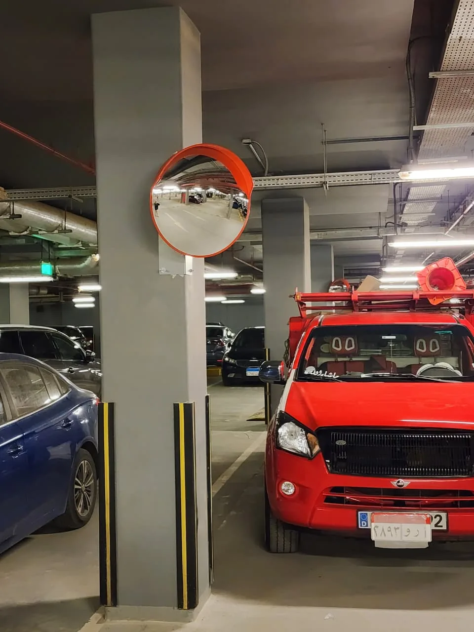 Convex safety mirror and yellow and black column corner guards in an underground car park