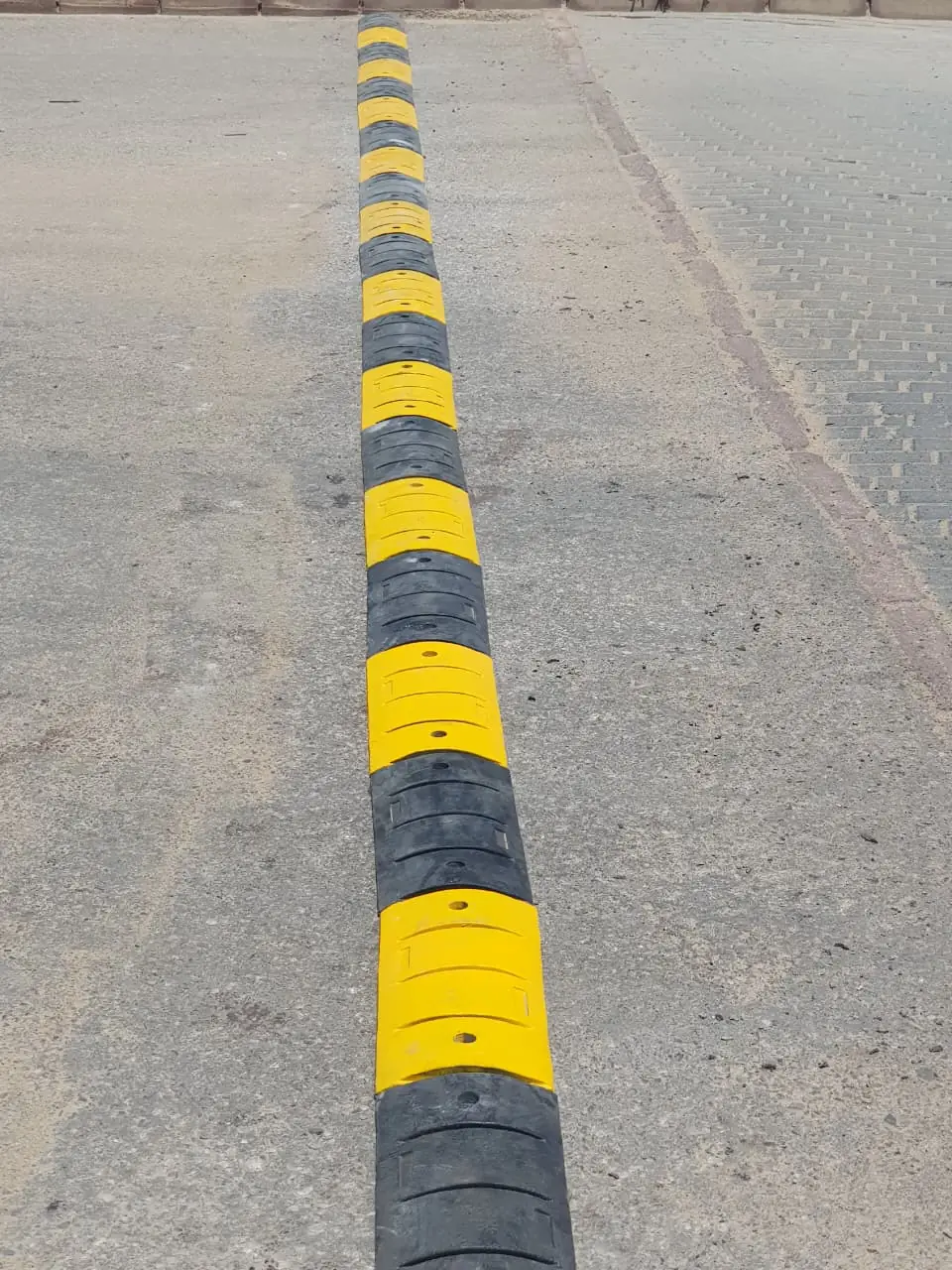 A full run of yellow and black modular rubber speed bumps installed across a road