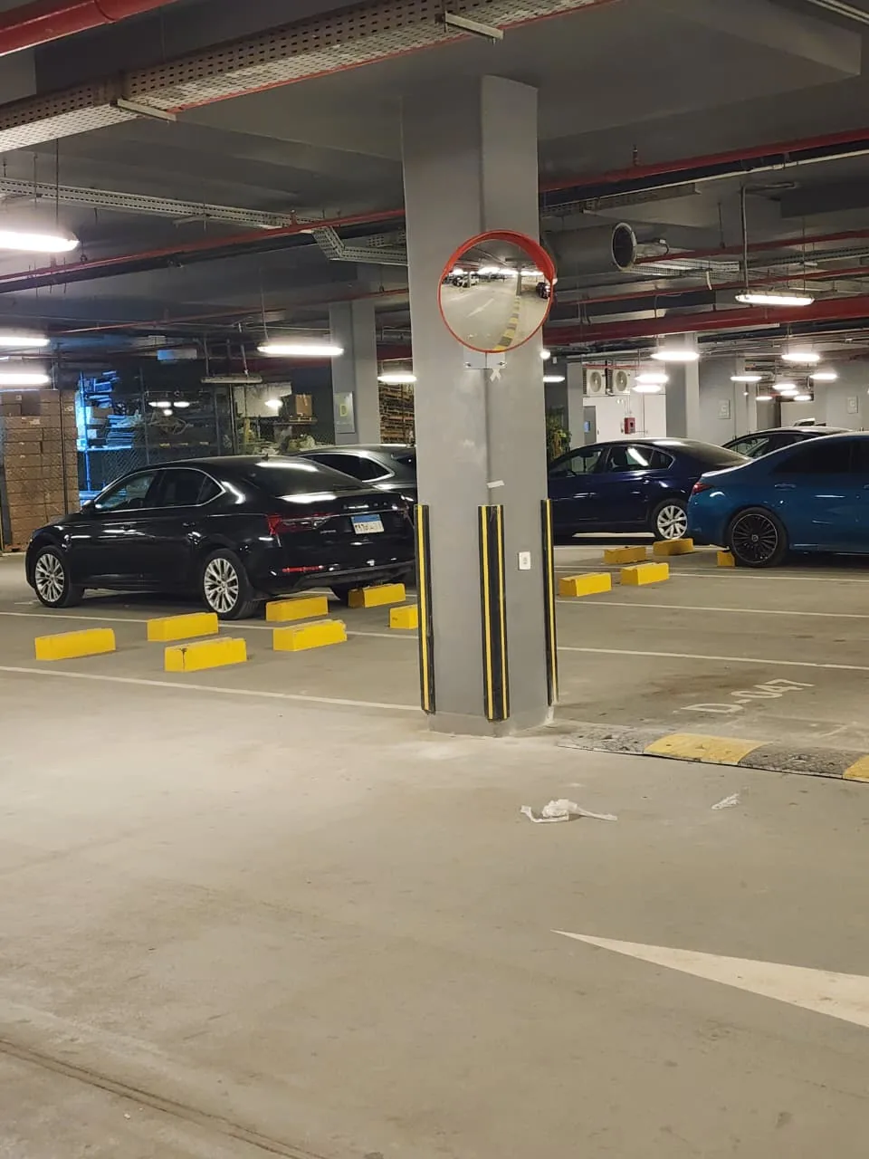 Yellow wheel stops, column corner guards and a convex mirror in an underground car park